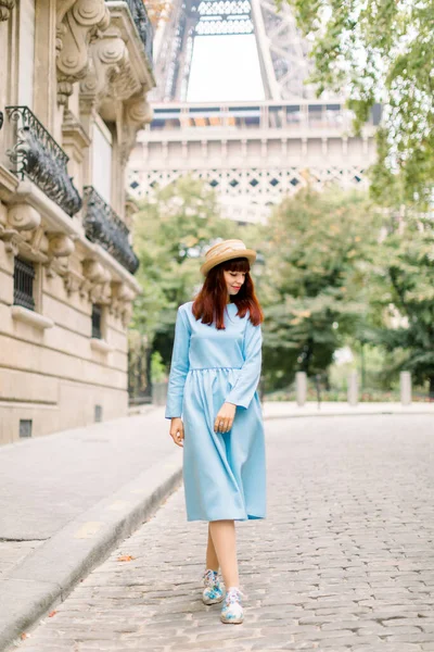 Bella turista donna, indossa un cappello elegante e vestito blu, camminando sulla strada accogliente con vecchi edifici d'epoca nella vecchia città europea di Parigi, con la torre Eiffel sullo sfondo — Foto Stock