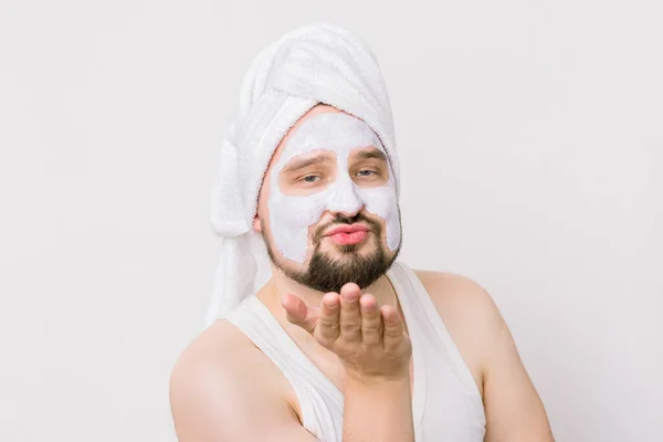 Emotional funny man having white cleansing mask after taking a shower in the morning, looking at camera and making air kiss. Close up portrait, isolated on white — Stock Photo, Image