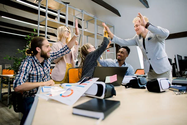 High-five för framgång. Olika grupp av fem affärskollegor ger varandra high-five i en symbol för bra jobb och leende när de arbetar i det moderna kontorsrummet — Stockfoto