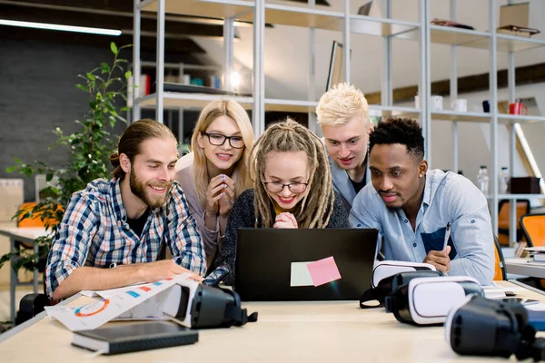 Grupp av unga mångsidiga multiracial designers som arbetar som team i moderna kreativa kontor. Ungdomar som arbetar tillsammans på bärbar dator håller sig lugna och väntar på resultat av sin gemensamma start-up. — Stockfoto