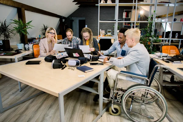 Modern ofiste, tekerlekli sandalyede birlikte çalışan beş genç, yaratıcı, etnik çeşitliliğe sahip iş adamı. Başarılı engelli iş adamları Telifsiz Stok Fotoğraflar