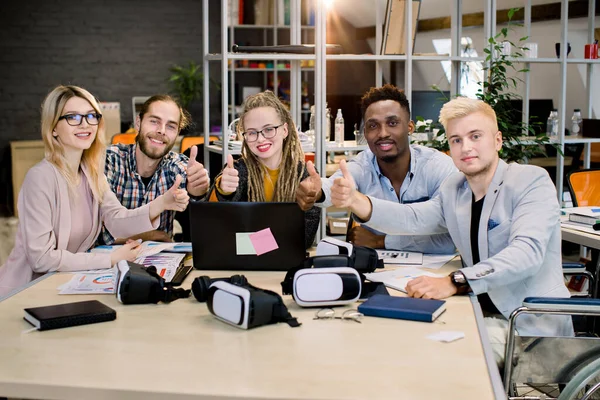 Kollektivt arbete för fullvärdiga personer och personer med funktionshinder. Multietniska ungdomar sitter i ämbetet och visar tummen upp. Personer med funktionsnedsättningar i vardagen. Affärsman med funktionshinder — Stockfoto