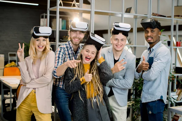 Fem glada multietniska vänner som njuter av sitt arbete med VR-glasögon i det moderna kreativa kontorsrummet. Ungdomar poserar med vr headset leende och gester till kameran — Stockfoto