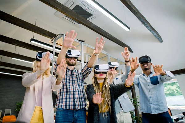 Glad multietniskt team av ungdomar i casual färgglada kläder försöker virtual reality glasögon för arbete i kreativa kontor. Ungdomar som använder ny teknik för start, 3D-visualisering — Stockfoto
