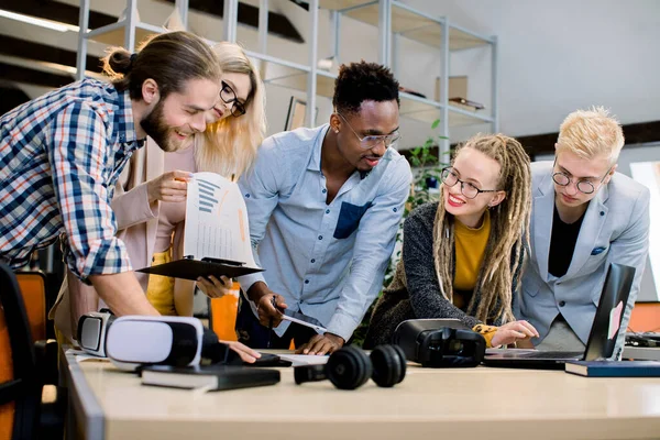 Boldog fiatal üzletemberek soknemzetiségű csoportja dolgozik együtt a hivatalban. Laptop, vr síszemüveg — Stock Fotó