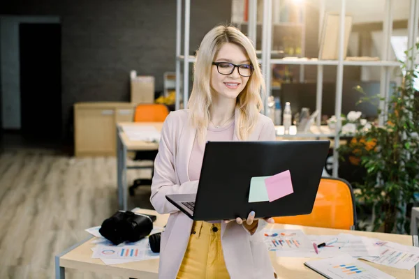 밝은 현대 사무실에서 노트북으로 일하는 젊고 아름다운 백인 사업가. 사무실에서 노트북으로 일하고 있는 예쁜 여자가 이 프로젝트를 끝내기 위해 — 스톡 사진