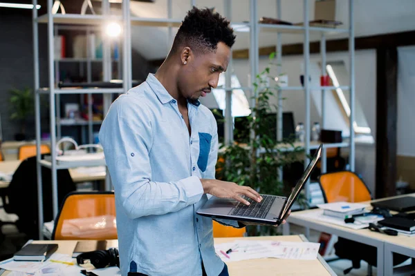 Professional concentrated African black man in office with laptop computer, having business call with clients. Male economist searches needed information, analyzes financial market