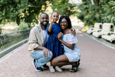 Açık havada yaz aile portresi. Güzel, Afro-Amerikan bir aile ve küçük tatlı bir kızları var. Park alanında poz veriyorlar, birbirlerine sarılıyorlar ve kameraya bakıyorlar.