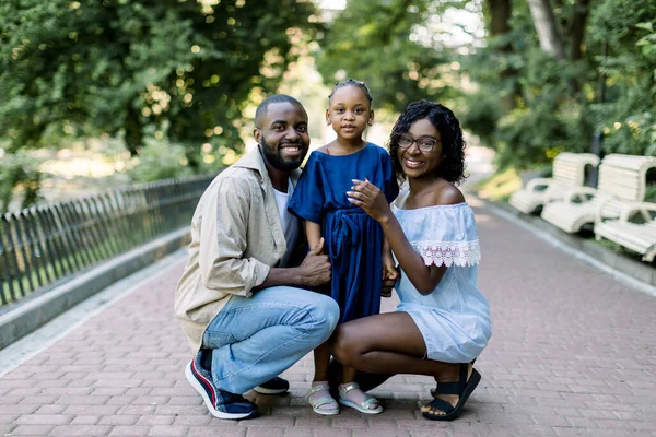 Retrato familiar de verano en la naturaleza al aire libre. Hermosa familia afroamericana joven con una linda hija pequeña, posando en el callejón del parque, abrazándose y mirando a la cámara — Foto de Stock