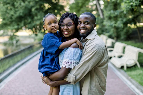 Jovem família africana feliz de três, pais e filha bonita, se divertindo juntos ao ar livre no parque da cidade, olhando feliz e sorriso. Felicidade e harmonia na vida familiar. Diversão familiar fora . — Fotografia de Stock