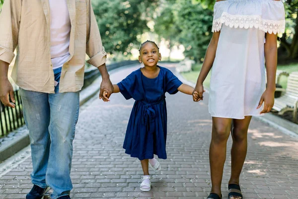 Imagen recortada de la adorable niña africana con un elegante vestido azul, caminando con sus padres en el parque al aire libre, tomados de la mano de padre y madre. Familia feliz y la infancia — Foto de Stock