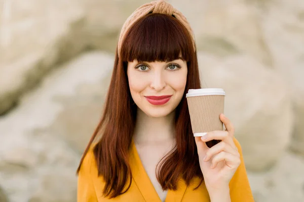 Close up portrait of beautiful cute smiling girl looking at camera while posing on the background of sand quarry or canyon and drinking coffee to take away, enjoying warm summer day — Stock Photo, Image