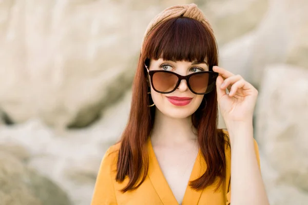 Draußen Nahaufnahme Porträt einer jungen schönen Frau mit perfekter Haut trägt gelbes Hemd, elegante Sonnenbrille, Haarband, posiert auf Sandsteinbruch, bei Sonnenuntergang. Kopieren, leerer Raum für Text — Stockfoto