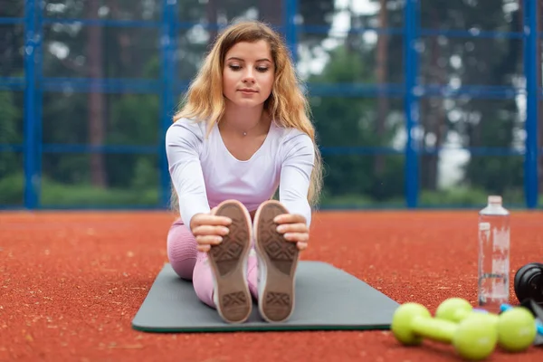 Front view of beautiful fit yoga woman in pink sportswear is practing yoga stretch pose sitting on yoga mat outdoor στο γήπεδο. Άσκηση, αθλητισμός, άνθρωποι και έννοια του υγιεινού τρόπου ζωής — Φωτογραφία Αρχείου