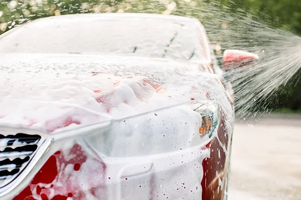 Lavar un coche con un cepillo y espuma de jabón antes de limpiarlo con un  chorro de agua al aire libre