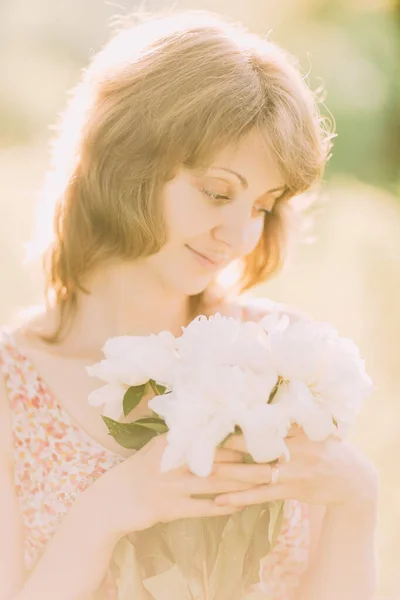 밝은 옷을 입고 하얀 콩으로 만든 꽃다발을 들고 여름들 판을 거닐거나 해질 녘에 정원을 거닐고 있는 아름다운 코카서스 의젊은 금발 여인. 밖에 꽃이 피는 여자 — 스톡 사진