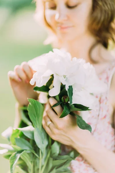 Mulher loira branca bonita em vestido leve segurando buquê de peônias brancas, andando no campo de verão ou jardim ao pôr do sol. Mulher com flores ao ar livre — Fotografia de Stock