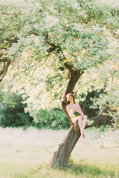 Mulher loira branca bonita em vestido leve segurando buquê de peônias brancas, andando no campo de verão ou jardim ao pôr do sol. Mulher com flores ao ar livre — Fotografia de Stock