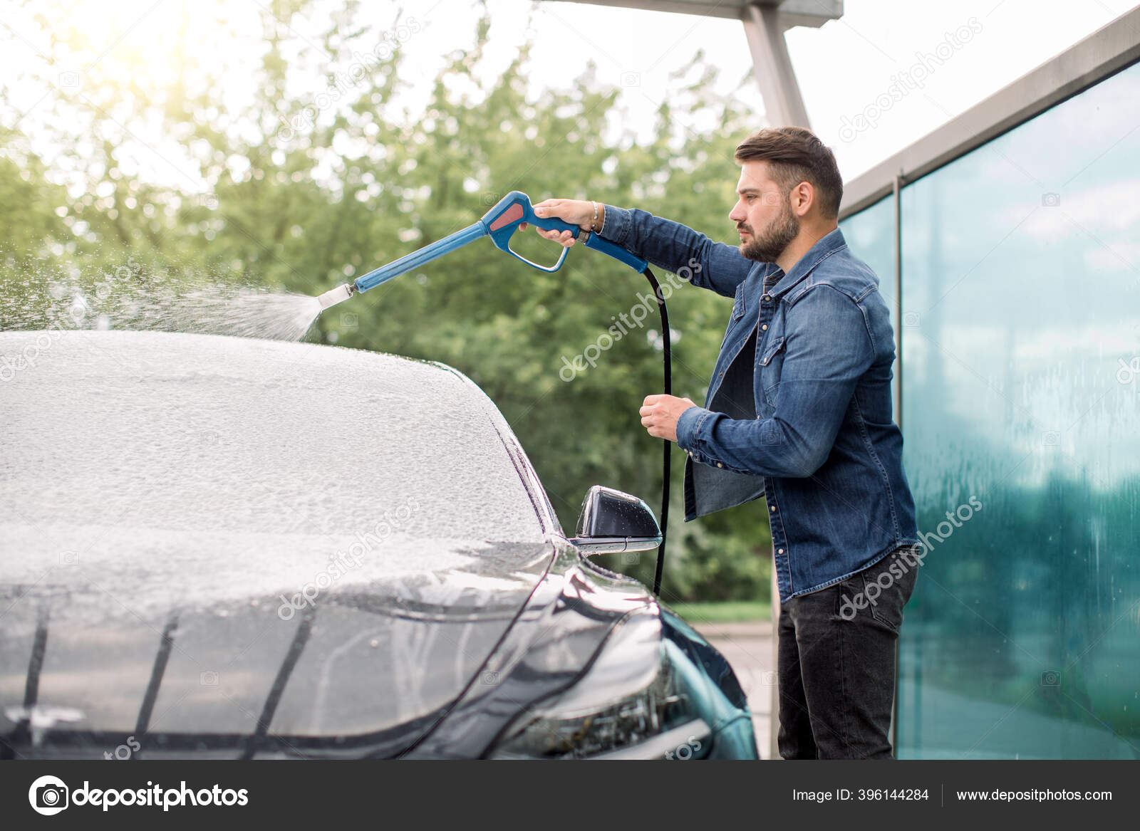 Joven hombre caucásico guapo limpiando su coche de lujo con aerosol de  espuma en la estación