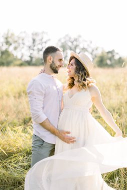 Yakışıklı sakallı adam ve hamile güzel karısı gün batımında açık havada yürüyorlar. Romantik aile, hamilelik kavramı