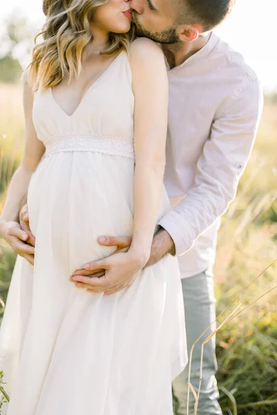 Yeşil bir yaz tarlasında beyaz elbiseli hamile kadınla mutlu bir adamın yakın çekimi. Hamilelik ve ebeveynlik. Sevgi ve bebek bekliyor. Hamile çift.. — Stok fotoğraf