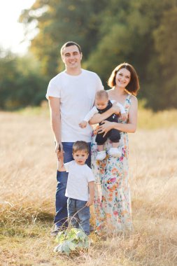 Çocuklarla dolu bir aile gün batımında yaz tarlasında yürüyorlar. Baba, anne ve iki çocuk yaz tarlasında eğleniyorlar. İnsanlar, aile günü ve yaşam tarzı konsepti