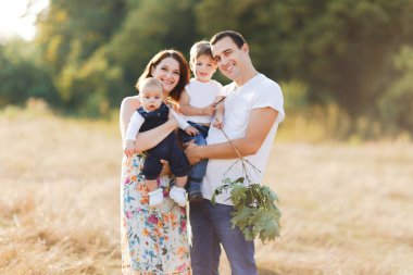 Çocuklarla dolu bir aile gün batımında yaz tarlasında yürüyorlar. Baba, anne ve iki çocuk yaz tarlasında eğleniyorlar. İnsanlar, aile günü ve yaşam tarzı konsepti