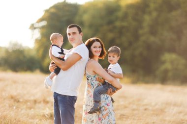 Çocuklarla dolu bir aile gün batımında yaz tarlasında yürüyorlar. Baba, anne ve iki çocuk yaz tarlasında eğleniyorlar. İnsanlar, aile günü ve yaşam tarzı konsepti