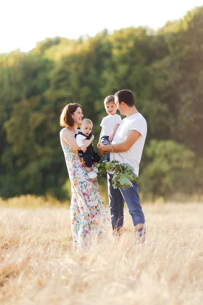 Família com crianças andando ao ar livre no campo de verão ao pôr do sol. Pai, mãe e dois filhos filhos se divertindo no campo de verão. Pessoas, dia de família e conceito de estilo de vida — Fotografia de Stock