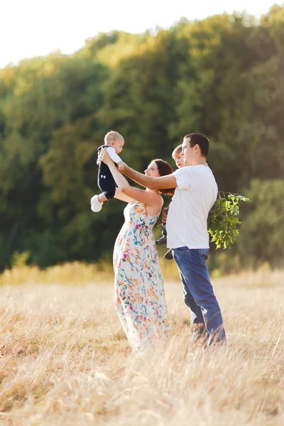 Família com crianças andando ao ar livre no campo de verão ao pôr do sol. Pai, mãe e dois filhos filhos se divertindo no campo de verão. Pessoas, dia de família e conceito de estilo de vida — Fotografia de Stock