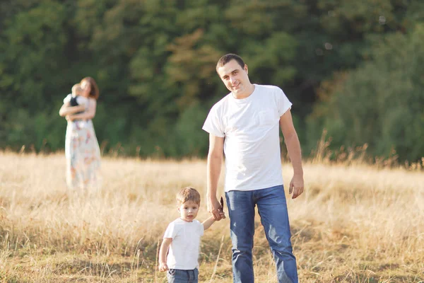 Família com crianças andando ao ar livre no campo de verão ao pôr do sol. Pai, mãe e dois filhos filhos se divertindo no campo de verão. Pessoas, dia de família e conceito de estilo de vida — Fotografia de Stock