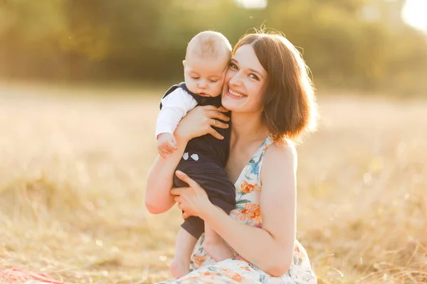 Família com crianças andando ao ar livre no campo de verão ao pôr do sol. Bonita jovem mãe e seu filhinho sentado na grama, se divertindo no campo de verão. Pessoas, dia de família e conceito de estilo de vida — Fotografia de Stock