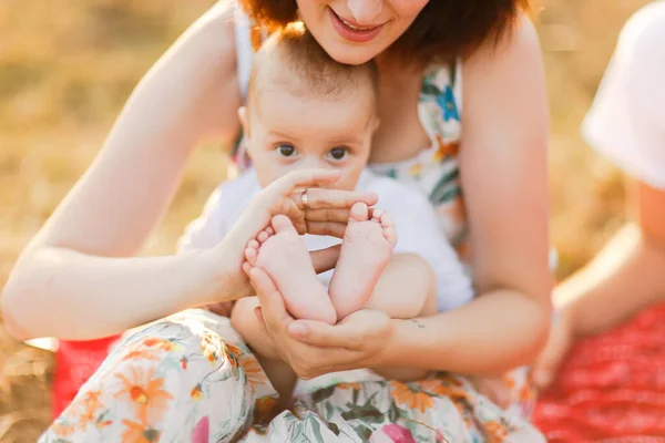 日没時に屋外で夏のフィールドを歩く子供連れの家族。幼い母親と小さな男の子が芝生の上に座って、夏のフィールドで楽しんでいます。人々、家族の日、ライフスタイルのコンセプト — ストック写真