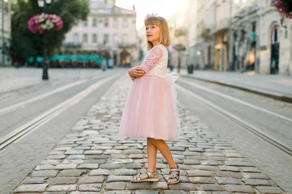 Маленька дівчинка в рожевій сукні принцеси виходить на вулицю і насолоджується видом на стародавній європейський центр міста. Життєпис маленької дівчинки, що ходить по місту. — стокове фото