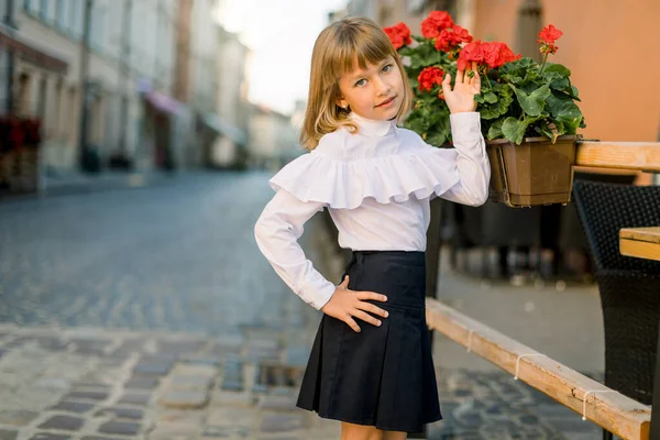 Close-up de pouco bonita menina branca loira tocando vasos de flores vermelhas decorações no dia de verão na antiga cidade europeia antiga — Fotografia de Stock