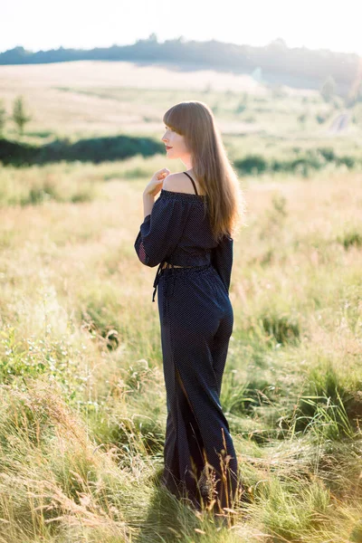 Jovem feliz elegante mulher de cabelos escuros em roupas pretas, desfrutando da natureza, posando em belo campo verde de verão ao pôr do sol. Menina bonita ao ar livre no campo — Fotografia de Stock