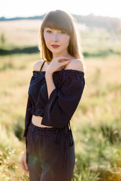 Mulher branca bonita em roupas pretas, posando para câmera no prado de verão ao pôr do sol — Fotografia de Stock