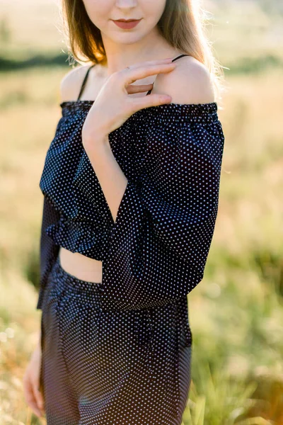 Cropped close up image de jeune femme heureuse en noir vêtements élégants, posant sur le coucher du soleil ou lever du soleil dans la nature d'été — Photo