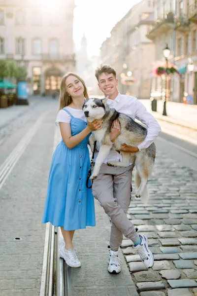 Веселий дружній знімок милої молодої пари зі своїм собакою, смішний сірий чоловічий собака, позує на камеру, що стоїть на трамвайній колії на тротуарній дорозі, в старовинному місті. Концепція сім'ї, тварин і людей — стокове фото