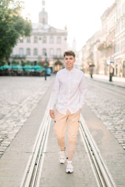 Yaz günü, şehir konseptinde yürüyüş. Beyaz gömlekli ve bej pantolonlu beyaz bir adam şehrin caddesinde dikiliyor.