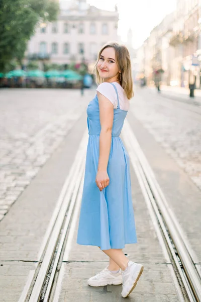 Retrato da menina branca bonita na moda vestindo vestido azul e tênis branco, andando na cidade europeia velha em um dia ensolarado de verão — Fotografia de Stock