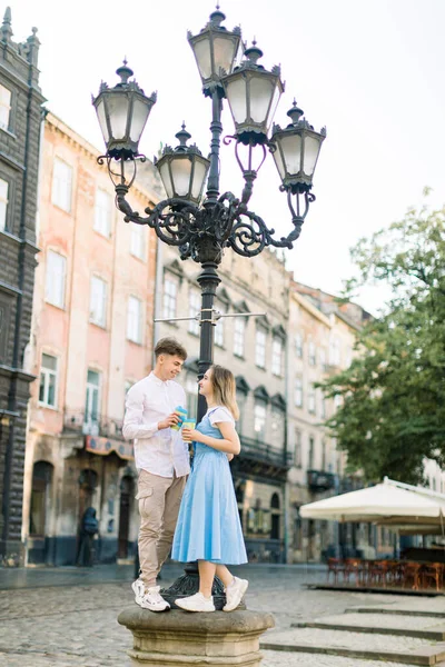 古い古代都市の屋外でロマンチックなデート。通りの光の下に立って、お互いを見て、コーヒーを取るのカップと恋に幸せな若いスタイリッシュなカップル — ストック写真