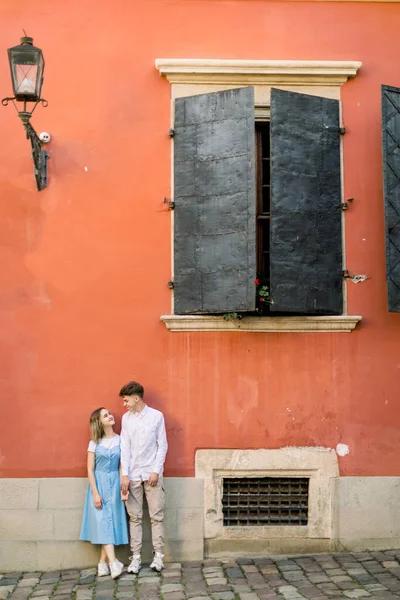 Portret van een verliefd koppel in de buurt van een oud vintage oranje gebouw. Gelukkig man en meisje in blauwe jurk, leunend op de muur van het oude gebouw en hand in hand — Stockfoto