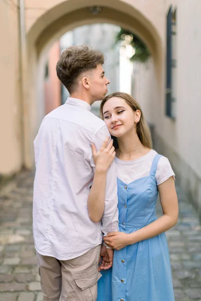 Romantic date outdoors in old European city. Portrait of stylish young couple in love, man in white shirt and girl in blue dress, posing to camera, while walking in the city. — Stock Photo, Image
