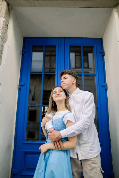 Lovely date on the street. Happy hipster young couple, handsome man with his attractive girlfriend in blue dress, hugging outdoors in the city, posing near beautiful vintage blue door — Stock Photo, Image