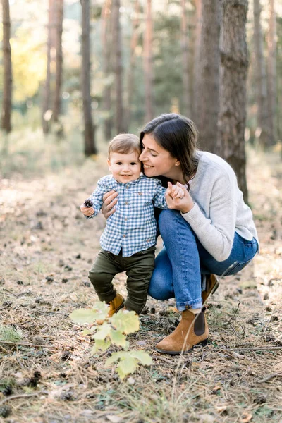 Genç bir aile, mutlu bir kadın anne çocuğuyla sonbahar çam ormanında eğleniyor. Anne parkta yürürken oğluna sarılıyor. — Stok fotoğraf