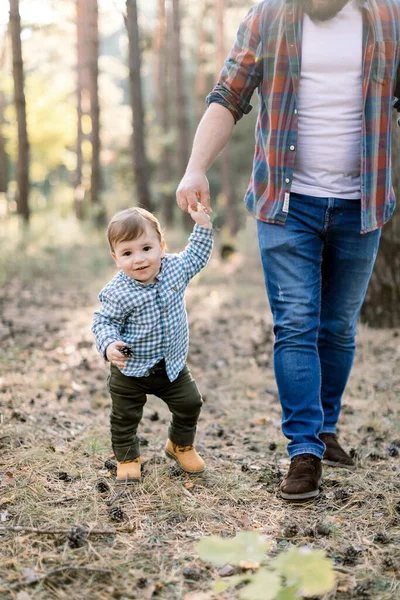 Feliz paternidade e conceito de caminhada familiar. Imagem cortada de menino pequeno andando junto com seu jovem pai bonito em roupas casuais elegantes na bela floresta no outono — Fotografia de Stock