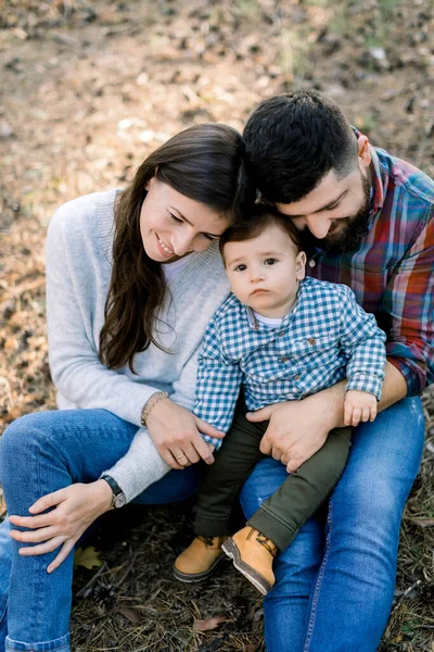 Güz parkında ya da ormanda, küçük bebeğe sarılan, birlikte oturup, dışarıda oynayarak eğlenen sevimli ebeveynlerin resmi. Sonbahar doğasında mutlu bir aile — Stok fotoğraf