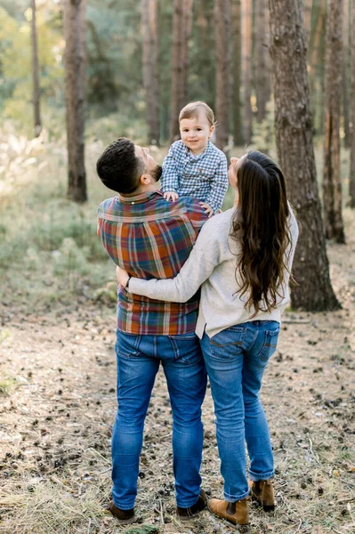 Genç ve şık ebeveynler, baba ve anne, küçük çocuklarını kucaklıyorlar, kameraya gülümsüyorlar. Açık hava aile portresi. Aile günü konsepti, çocukla yürümek. — Stok fotoğraf