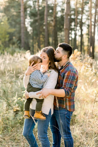 Baba, anne ve küçük oğlu günbatımında sonbahar çam ormanında yürüyorlar. Mutlu aile eğleniyor, sarılıp öpüşüyorlar, gün batımında doğada poz veriyorlar. — Stok fotoğraf